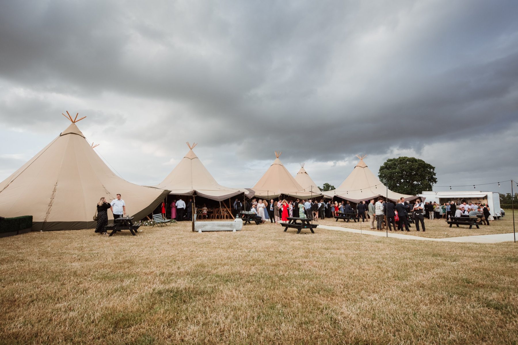 A large crowd outside five linked Java tipis with a catering trailer and picnic benches