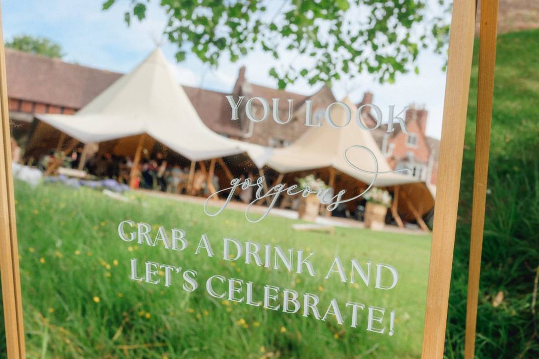 Two Java tipis on the lawn in front of a manor house, seen through a welcome mirror reading 'You look gorgeous, grab a drink and let's celebrate!'