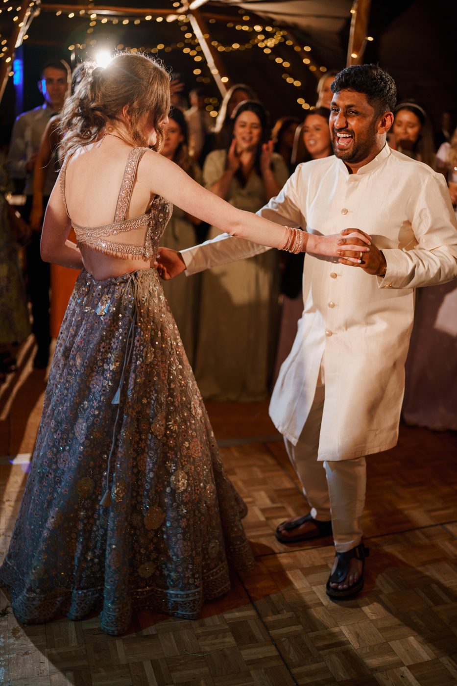 Ailish and Niku dancing together under fairy lights as their guests cheer