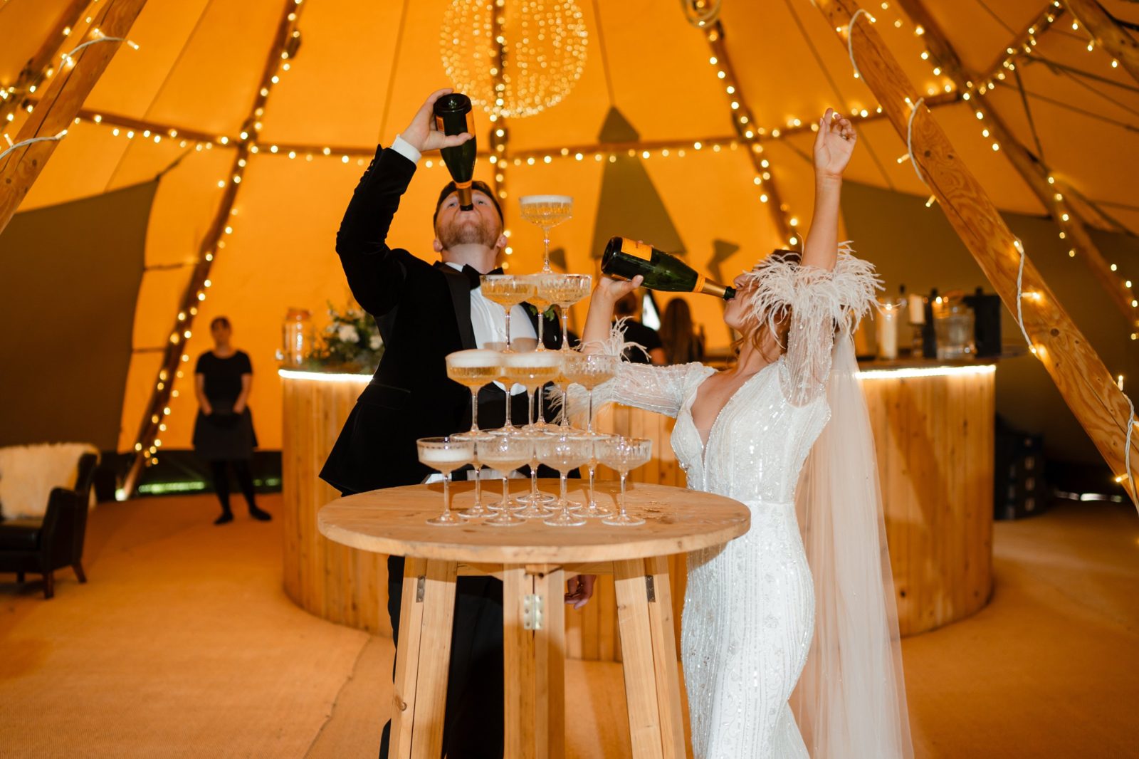 Bride and groom celebrating with champagne beside the Java mobile bar inside a lit tipi