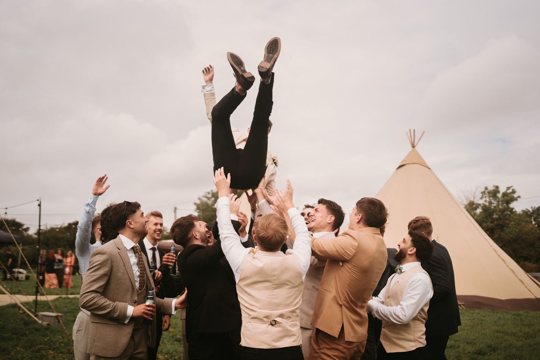 Groomsmen throwing the groom into the air beside a tipi