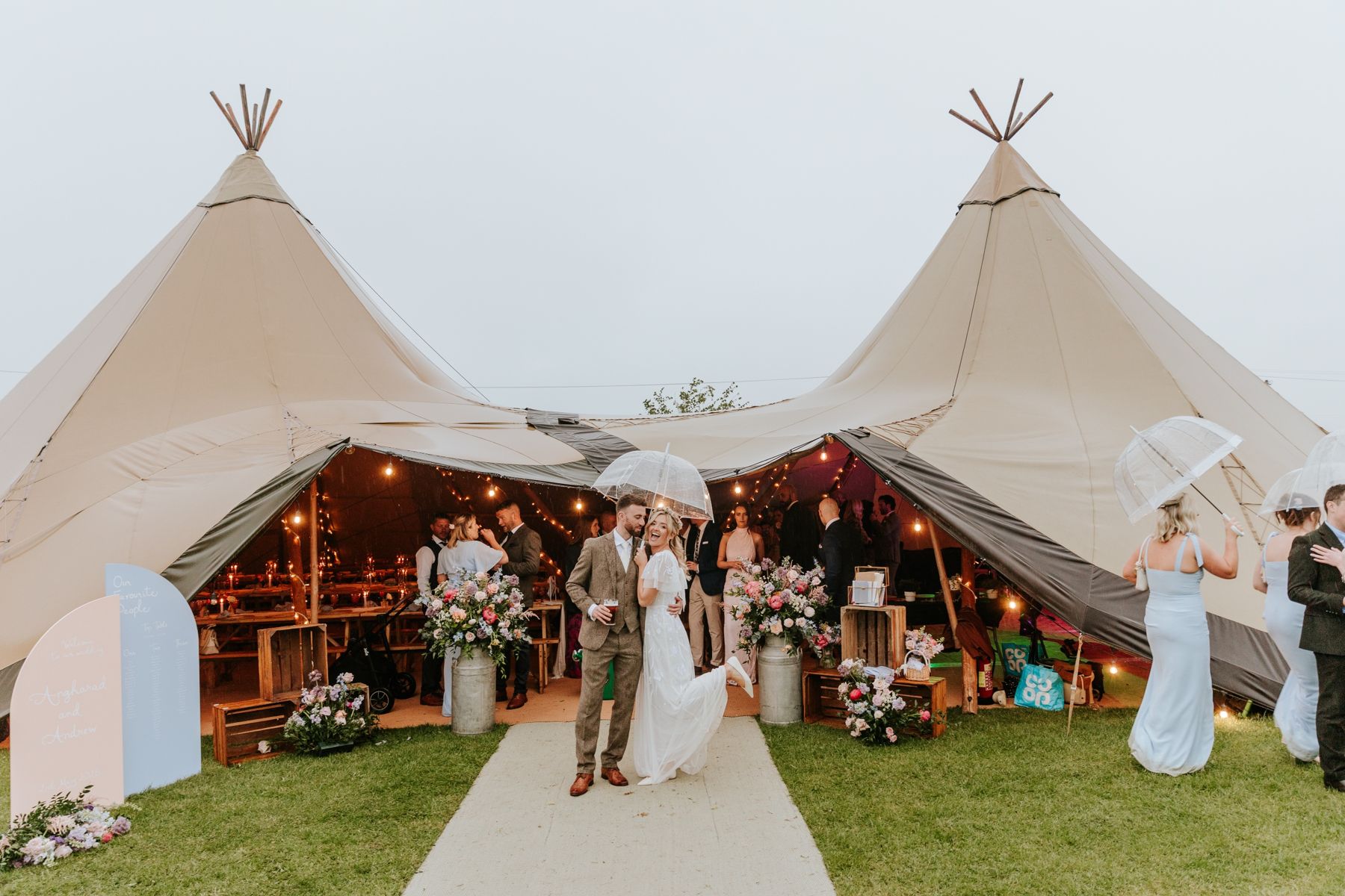 Haz and Andrew laughing under an umbrella outside their tipis