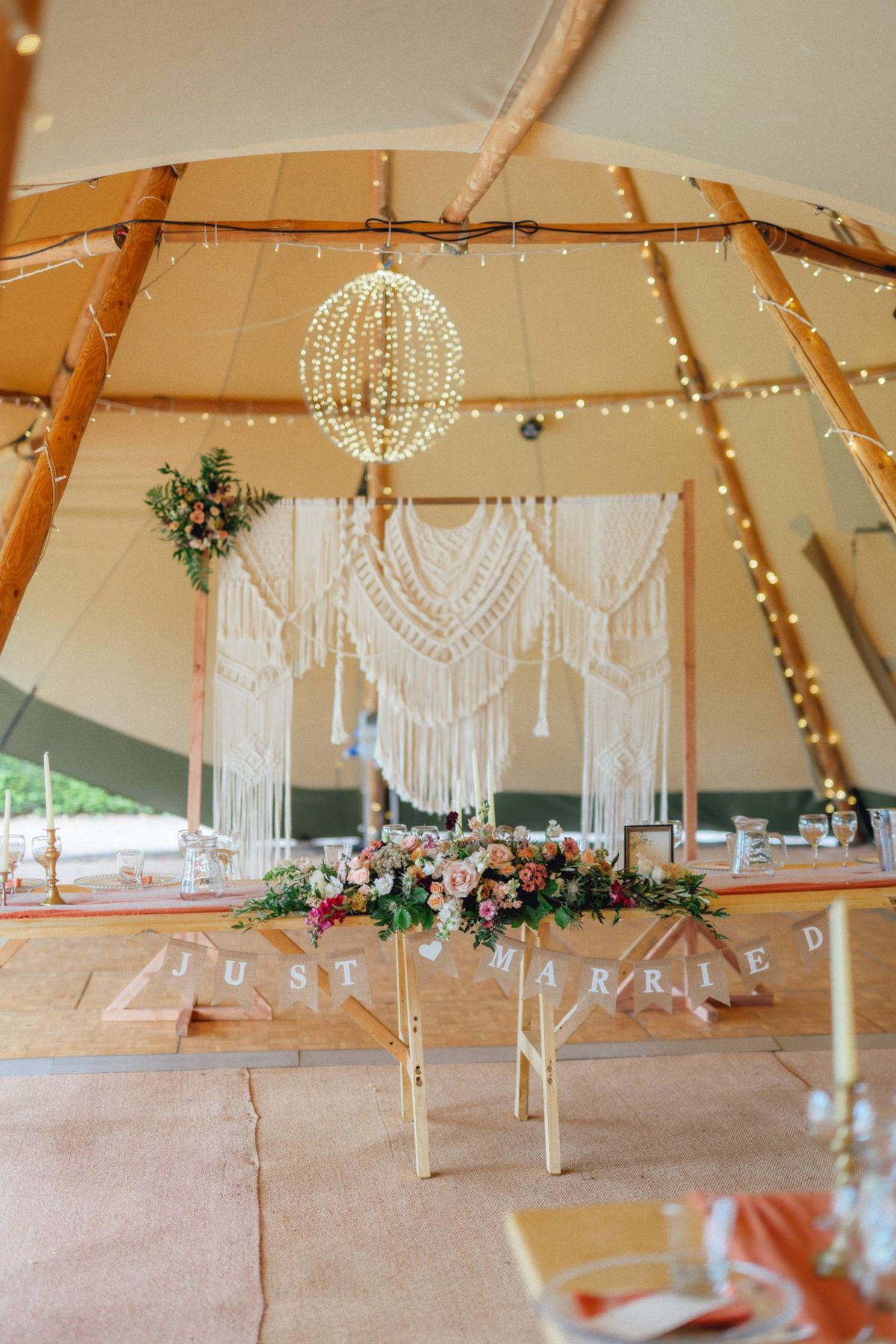 Tipi top table styled with a macramé backdrop, light orb, candles and Just Married bunting
